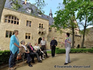 Gästeführerin mit Gruppe von Gästen, teils auf einer Bank sitzend unter Bäumen im Schlosshof. - Foto von Touristinfo Alzeyer-Land