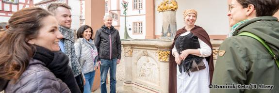 Stadtführerin erklärt einer Gruppe von Menschen den Brunnen am Fischmarkt